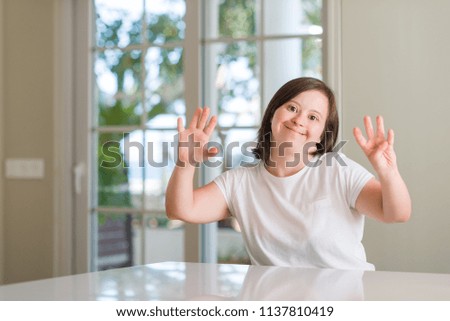 Down syndrome woman at home showing and pointing up with fingers number nine while smiling confident and happy.