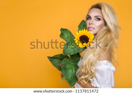 Beautiful woman posing with yellow sunflower on yellow pastel studio background. Concept of women's and mother's day. Spring, summer feelings. Girl power. Spring fashion.