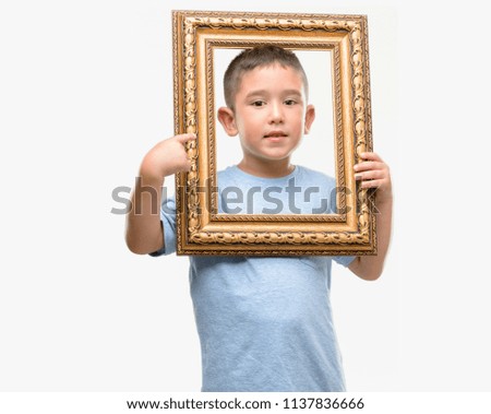 Dark haired little child holding frame very happy pointing with hand and finger