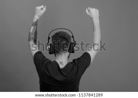 Relax and music concept. Singer enjoys music partying. Dj with scorpio tattoo wears headphones, copy space. Man holds hands up, dancing turned around on blue background.