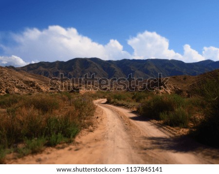 Dirt road running through a dry landscape towards mountains with dramatic clouds at fairytale canyon at lake Issul Kul