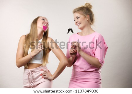 Two happy women holding symbols on stick having fun. Photo and carnival funny accessories concept.