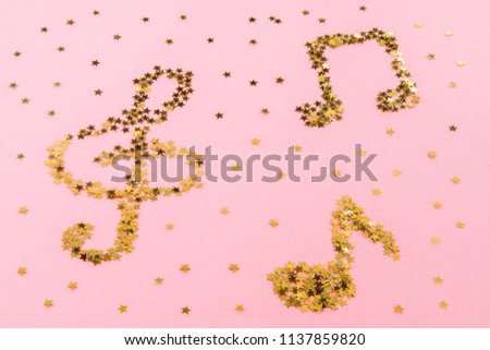 Musical notes of starry golden confetti lying on a pink pastel background.