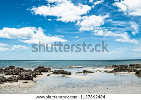Clear sky during the day.By the sea, sand and rocks.Sea picture reflects the sky.
