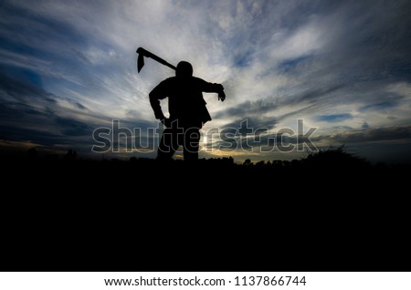 Thai farmer and he is carrying a hoe or weed tool at twilight time on rice field. Picture is silhouette style.