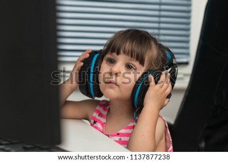 Cute little girl with large headphones sitting in front of a computer