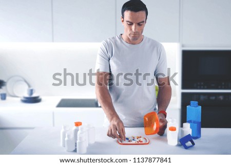 Responsible person. Calm concentrated young man paying attention to the condition of his health and carefully taking a pill from the plate