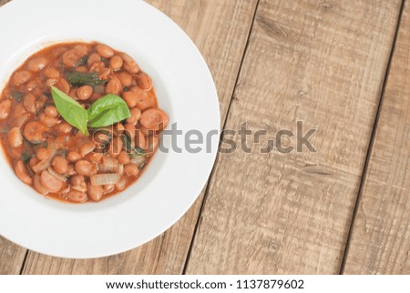 Cooked Red Beans in Tomato Sauce with Spinach and Onion, white Round Plate, Wooden Background, Top view, Copy space.