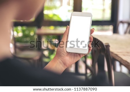 Mockup image of a woman holding white mobile phone with blank desktop screen in cafe