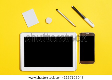 felt pen, pencil, rubber and paper stickers lying in front of smartphone and tablet pc at the yellow background. concept of office or educational stationary and gadgets. free copyspace. top view
