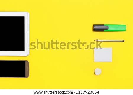 green bright marker, pencil, rubber and paper stickers lying against smartphone and tablet pc at the yellow background. concept of office or educational stationary and gadgets. free copyspace