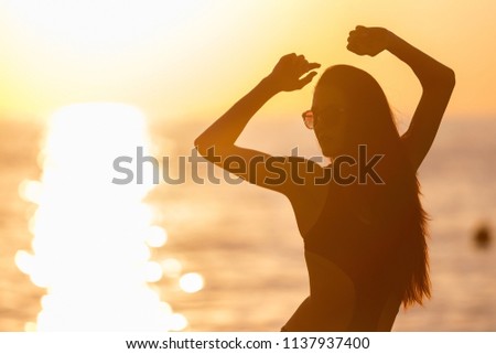 pretty young teen with long dark hair tanning in black swimwear against an ocean and sunset . concept of happy holiday and resort time. silhouette over sunrise