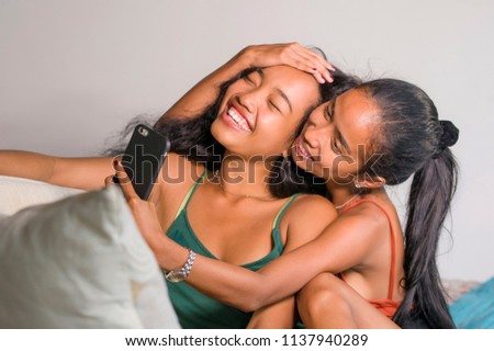 young happy and beautiful Asian sisters or girlfriends couple smiling cheerful taking selfie photo with mobile phone at home couch playful laughing together in female friendship lifestyle and love