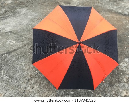 Black- orange rain umbrella  placed on a gray cement floor.