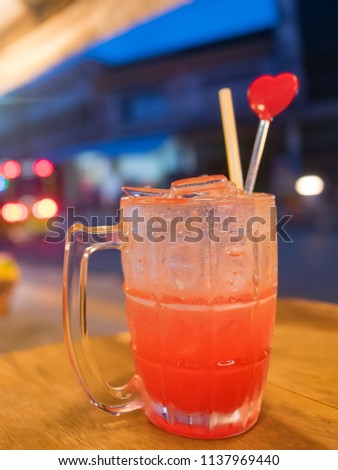 glass of ice soda strawberry punch soft drink with red heart cocktail stirrer swizzle sticks  and strow on wooden table