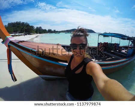 Travel/summer holiday concept.Young happy tourist european woman taking selfie photo with long tail boat on iddilyc white sand beach with turquoise water in Thailand. Enjoying vacation. Bright colours