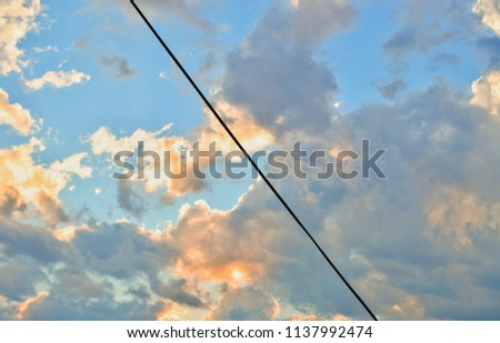 Sky with clouds. Sky of orange color with black cable crossing. Light cable in sky. Sky divided in two