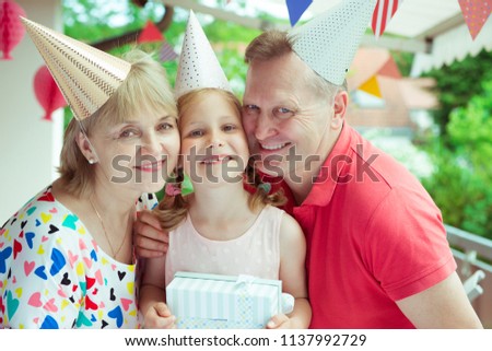 Portrait of happy grandparents celebrating birthday with their pretty little granddaughter on colorful decorated terrace