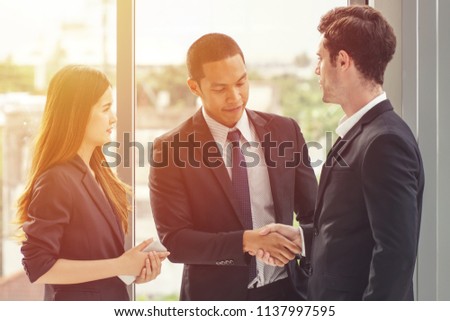 Two businessman shaking hands with a woman secretary/translator standing on the side.