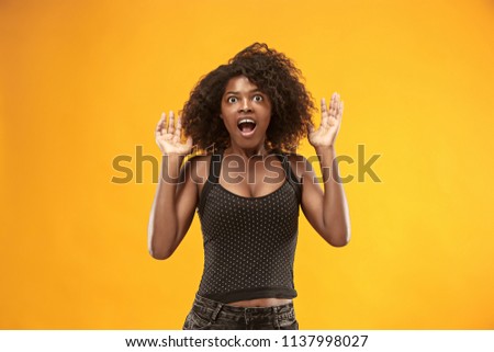 Wow. Beautiful female half-length portrait isolated on gold studio backgroud. Young surprised woman holding hands by head, looking at camera. Human emotions, facial expression concept. Trendy colors