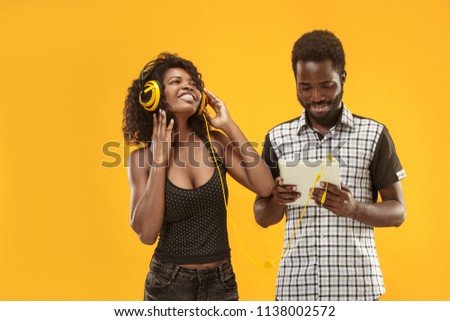 adorable curly girl happy smiling during photoshoot. Stunning african woman with light-brown skin and afro man relaxing in headphones and funny dancing on colorful yellow background at studio.