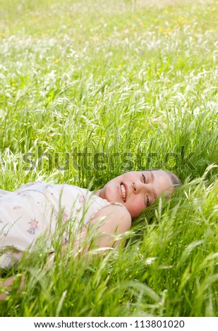 Young teenager laying down on a long green grass garden, smiling at the camera.