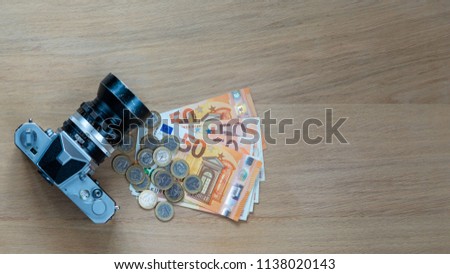 Euro banknotes, coins and a camera on a light wooden background.