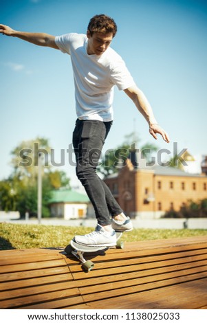 Young attractive man in white T-shirt riding longboard in the park.