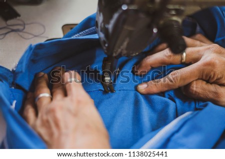 Woman hands sews clothes made of blue cloth on a sewing machine.