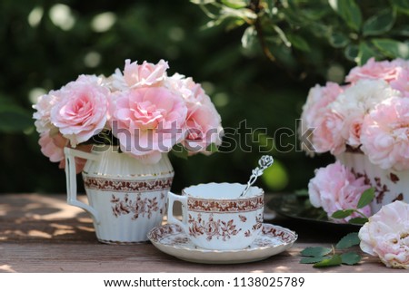 Beauty bouquet of roses in antique porcelain old sugar bowl, china tea cup, clover, thistle pattern with silver spoon on wooden table, vintage style, floral scene in garden, summer day
