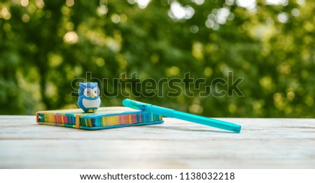 notebook, pen and owl toy on table, natural green background. symbol of knowledge. concept of teaching and school. minimal kawaii style. creative idea. copy space