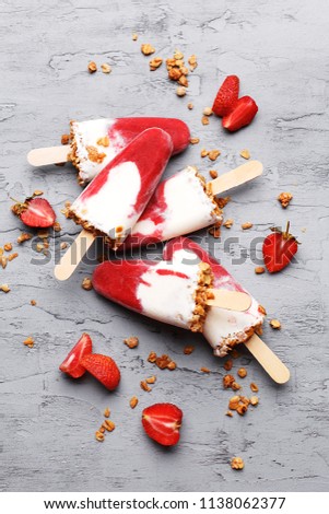 Homemade ice cream popsicles with strawberry and granola on gray concrete background. Top view