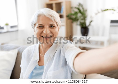 technology, communication and people concept - happy smiling senior woman in glasses taking selfie at home