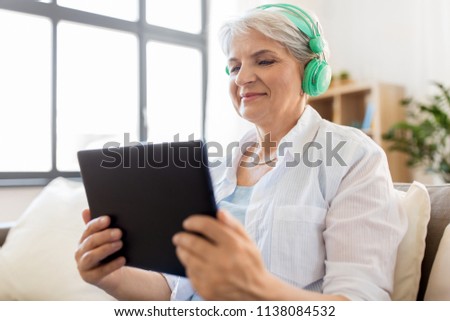 technology, people and lifestyle concept - happy senior woman in headphones and tablet pc computer listening to music at home