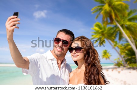 travel, tourism and summer vacation concept - smiling couple in sunglasses making selfie by smartphone over tropical beach background in french polynesia