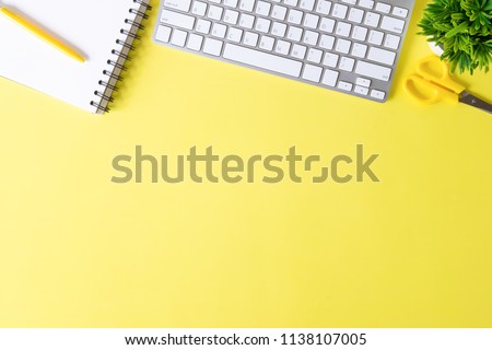Above Office desk with computer keyboard, notebook paper, pen and plant decoration on yellow background top view mock up.