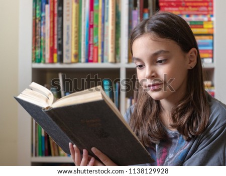 beautiful girl reads a dark book on the background of a bookcase