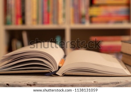 Notepad / book is on a wooden table. orange simple pencil. background, bookcase with colored books	