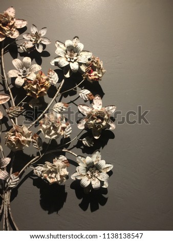 Flowers and leaves are made from steel on the wall, with the light from the top, creating a beautiful shadow on the wall. Background is the Gradient gray color.