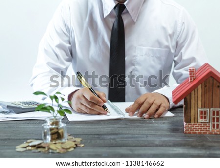 Business man hands pushing pen, calculating house design blueprint as a business and financial investment.Coin,a model of a wooden house.Planning of the construction of a house.