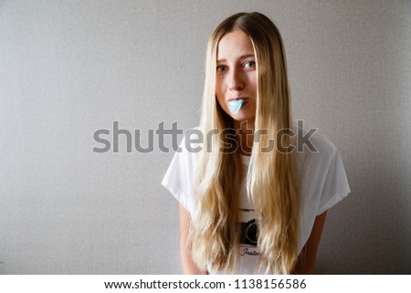 Portrait of beautiful young woman with blonde hair with bubble gum isolated on gray background