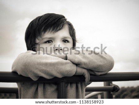 Black and white photo of lonely child standing alone in playground,Sad boy playing alone at the park,Poor kid with thinking face looking out waiting for some one at play area