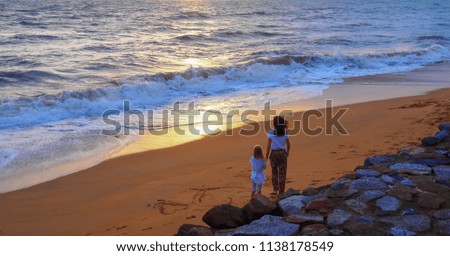 mother and daughter walking on the beach at sunset. 