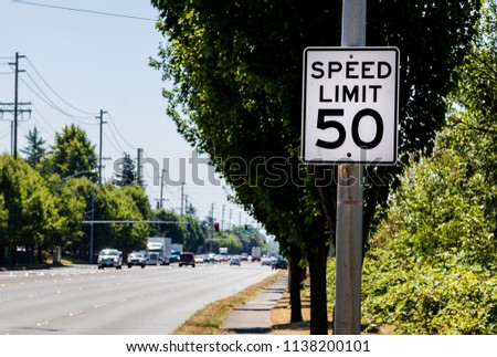 50 mph speed limit sign on post with a road and tree with bushes