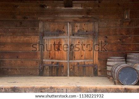Old wooden double doors with rusty weathered hardware, wooden barrels stacked beside door.