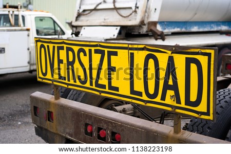 Black on yellow oversize load sign Installed on the back of big rig semi truck tractor with heavy metal bumper for safety moving stand on the parking lot awaiting for the next oversized cargo