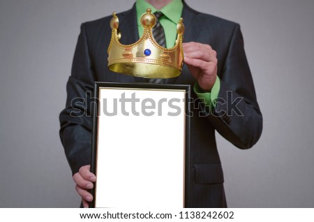 Winner blank diploma or certificate mockup in businessman hand. Man is holding a blank photo frame with copy space for human face and a golden crown above it.