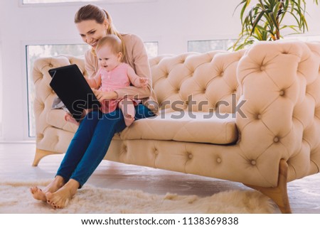 Watching cartoons. Cheerful kind young mother holding a modern tablet while showing funny cartons to her little child
