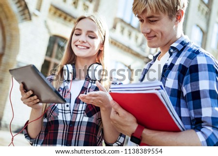 Great mood. Pretty blonde keeping smile on her face and looking downwards, holding her gadget in right hand