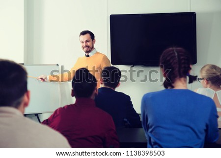 male and female students following explanations of smiling teacher in class